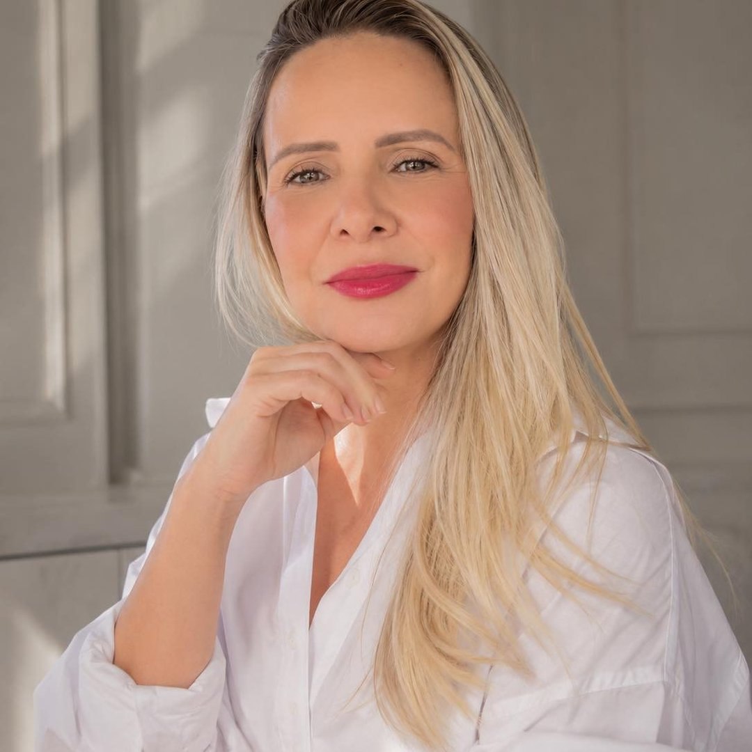 Retrato de Rita Camargo, profissional de skincare, sorrindo em ambiente claro com camisa branca
